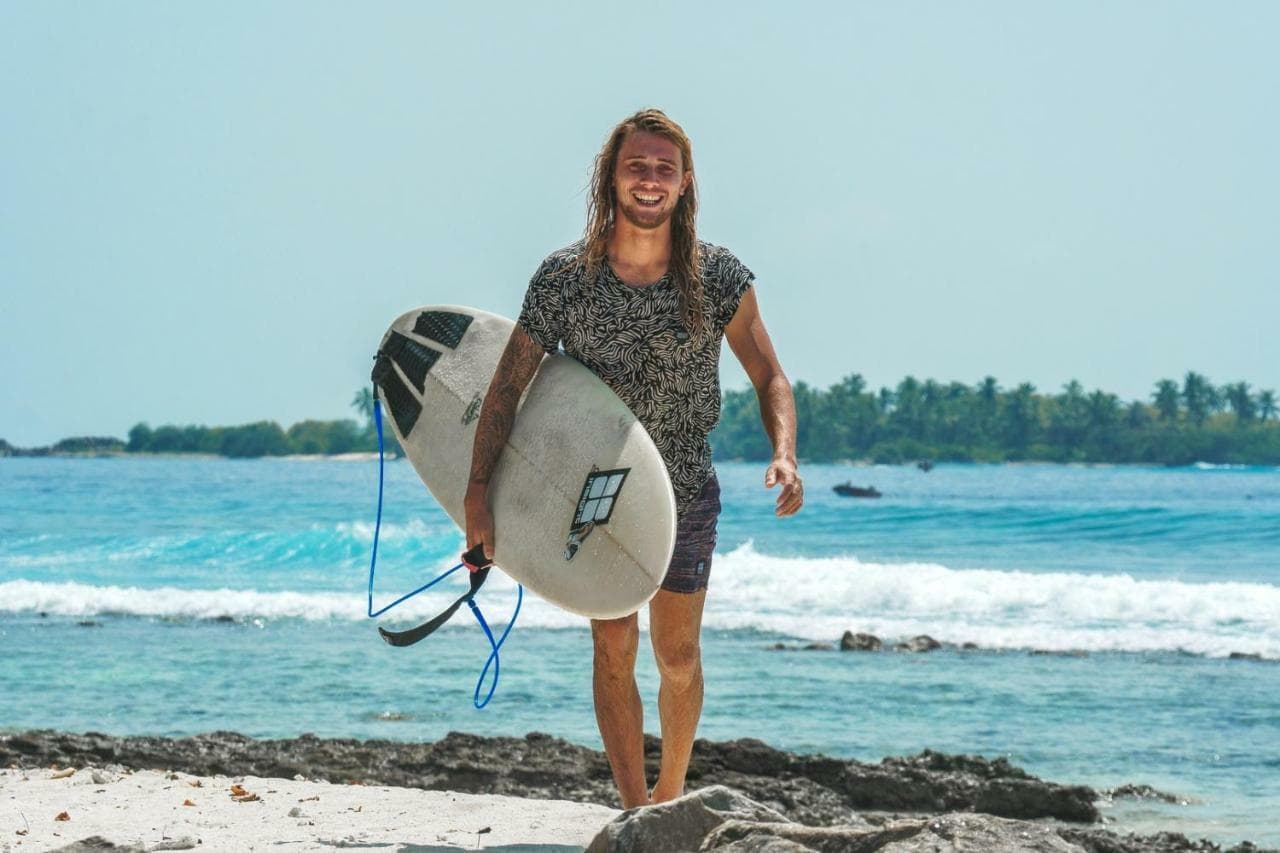 Surfer carrying his board across the reef flat near Himmafushi