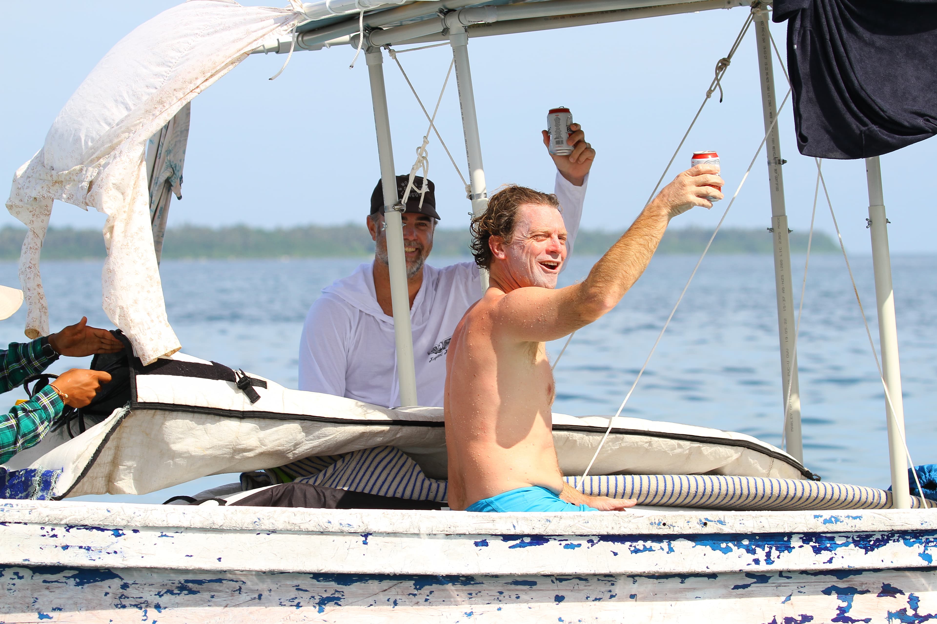 Guest smiling from a boat and holding up cold drinks near Asu Island