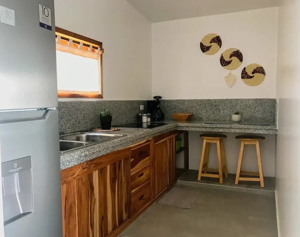 A kitchen with teak cabinets, a stone counter and two stools