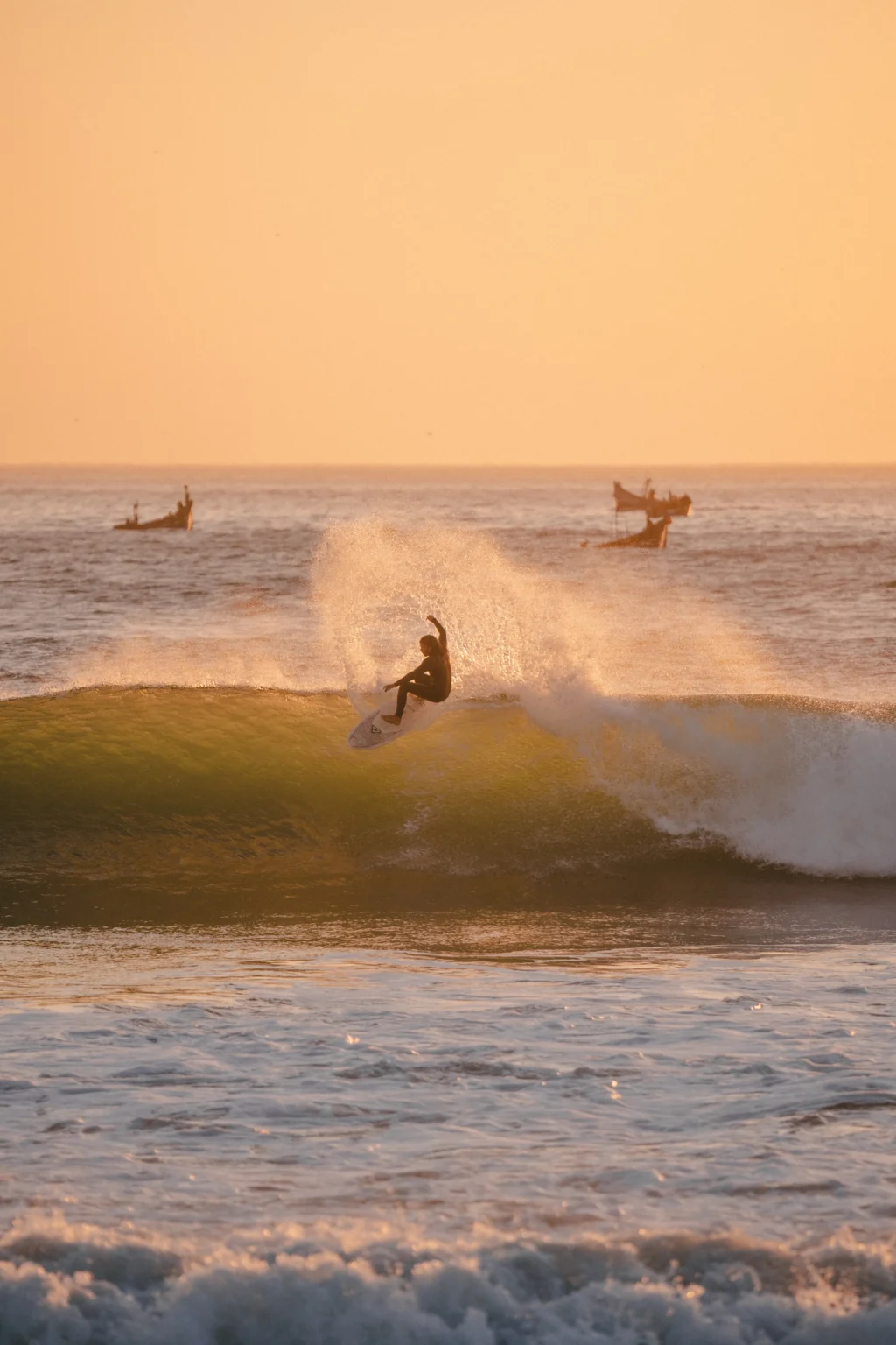 A surfer turning off the top of a wave at Imsouane with fishing boats sitting outside
